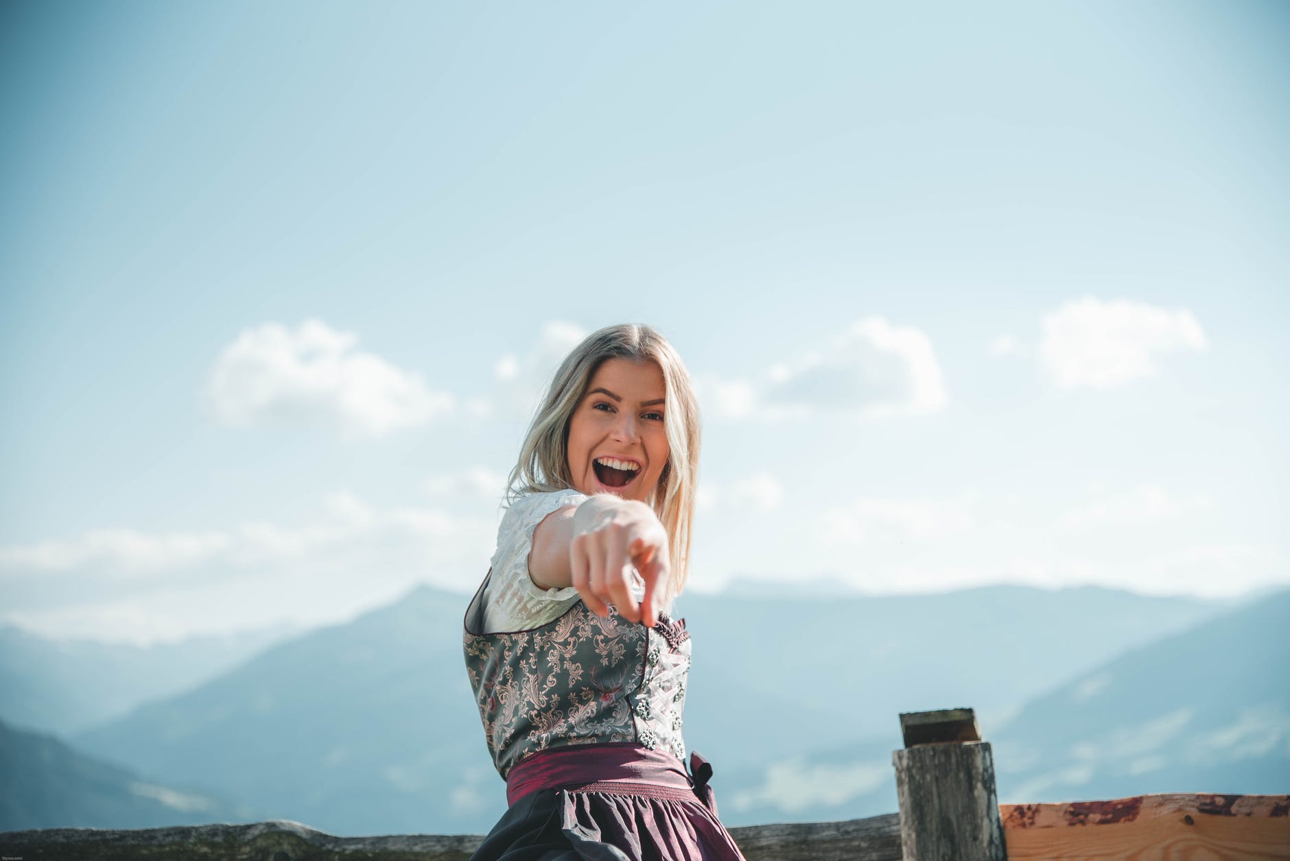 smiling woman wearing floral dress pointing with right hand